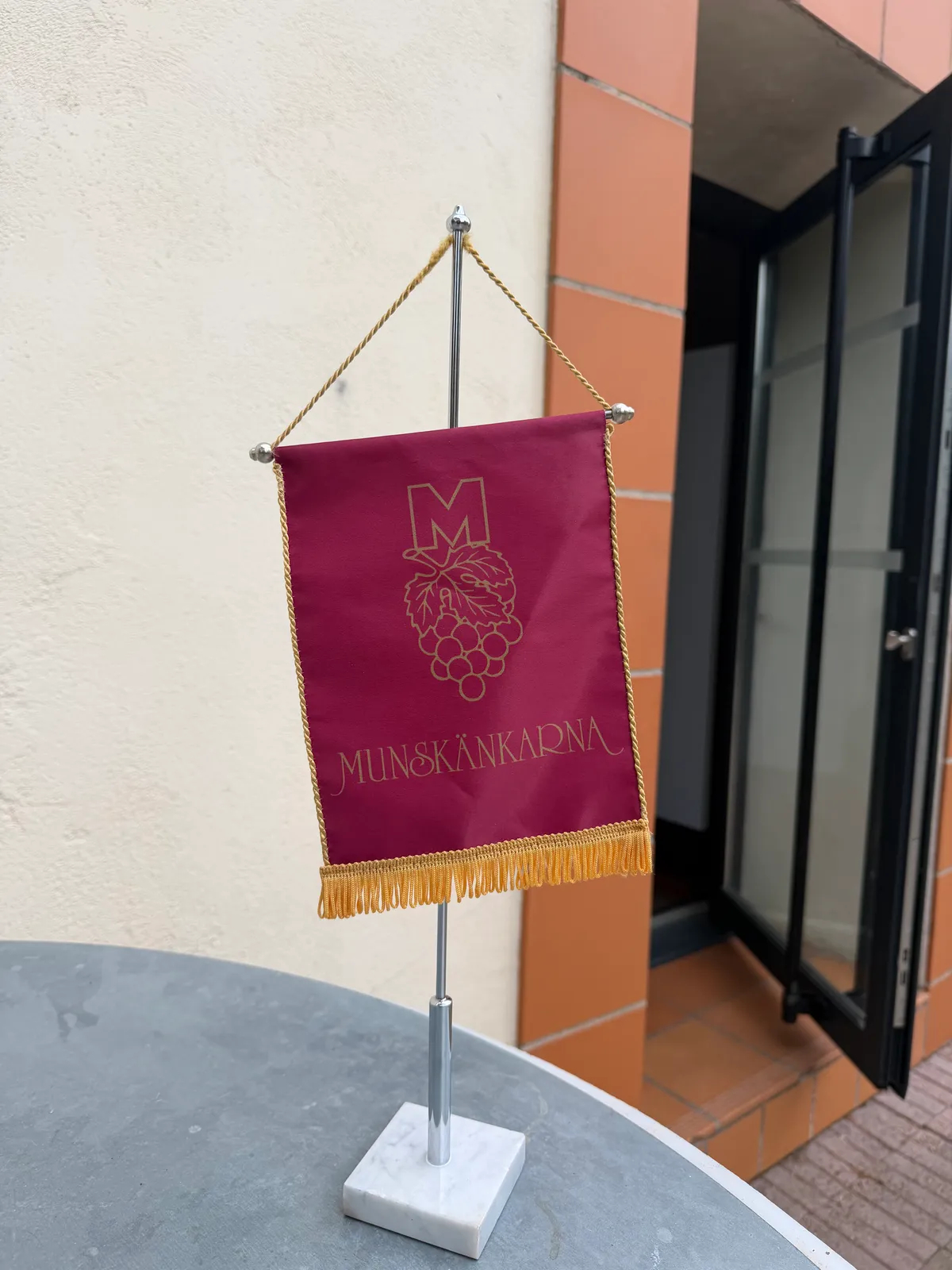 Munskänkarnas bordsstandar i vinrött med guldbroderad logotyp, på ett bord utanför lokalen