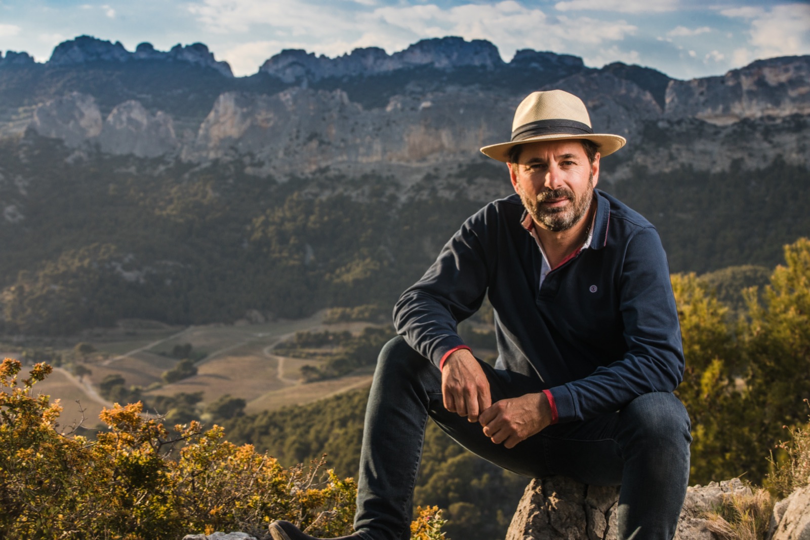 Xavier Vignon sittande på en klippa framför Dentelles de Montmirails taggiga kalkstenskam, med vingårdarna i dalen nedanför